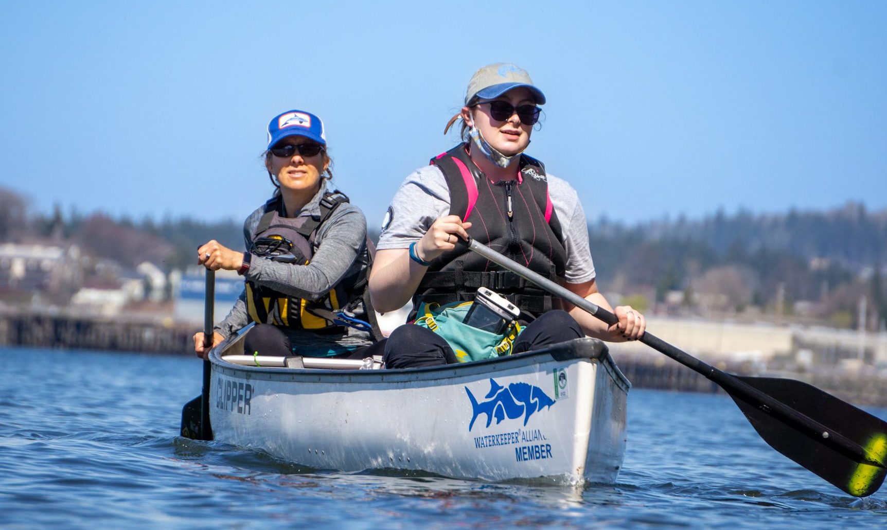 Two people paddling a canoe on Bellingham Bay with the shoreline in the background