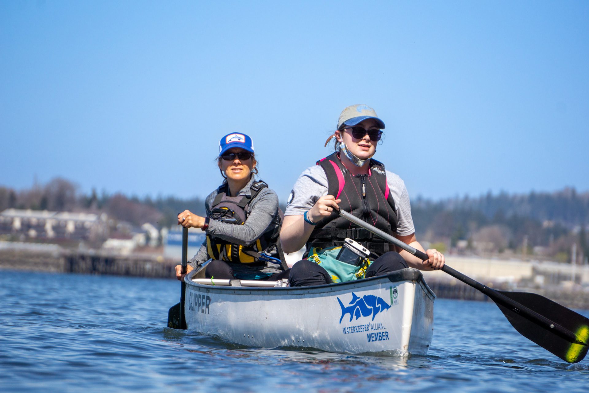 Two people paddling a canoe on Bellingham Bay with the shoreline in the background