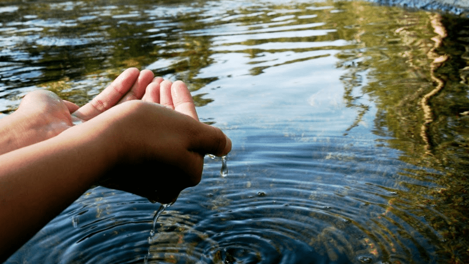 Two hands cupping water over a river