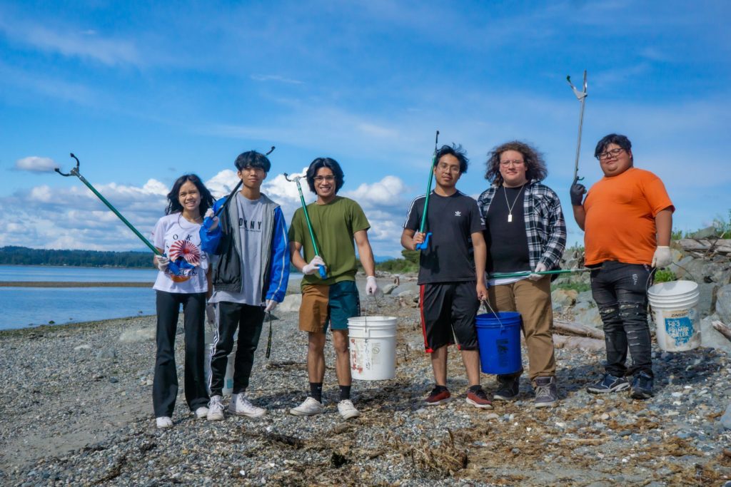A group of young people with trash grabbers standing on the beach along Semiahmoo Spit