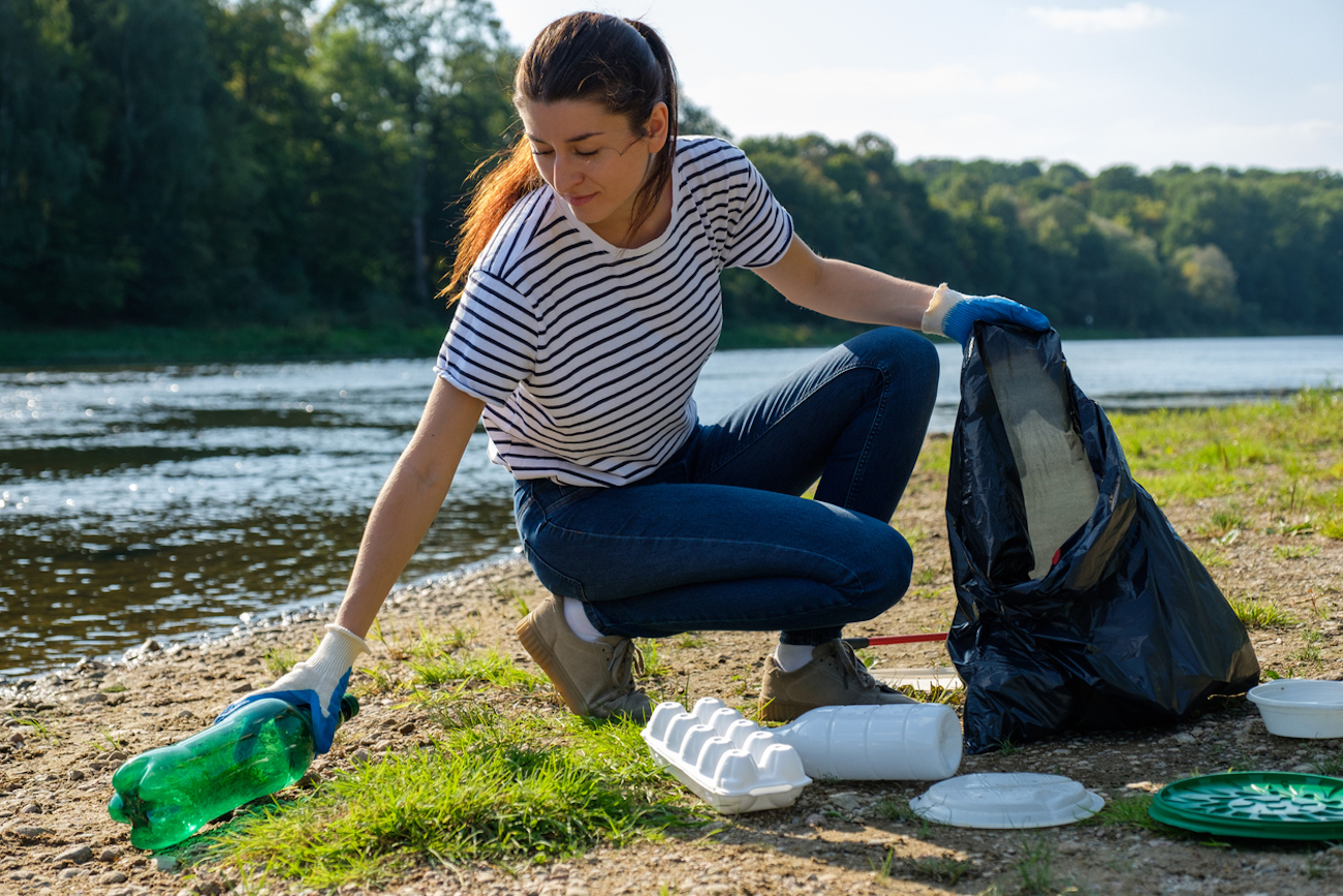 Volunteer woman collecting plastic rubbish on bank of the river.